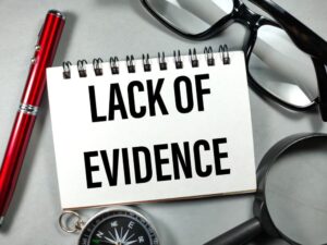 The central focus is on a note that reads 'LACK OF EVIDENCE.' The image is intentionally styled with noise and film grain for a vintage aesthetic."