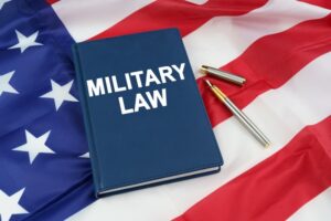 On the US flag rests a pen and a book labeled "MILITARY LAW". 