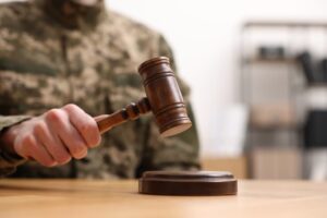 Law concept. Closeup of a man in military uniform holding a gavel at a wooden table. Space for text.