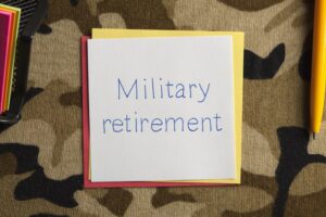 Top view of a note about military retirement placed on a camouflage fabric background. 