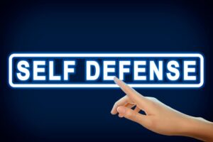 A close-up shot captures a woman pointing at the words 'Self Defense' displayed on a virtual screen against a vibrant blue background.