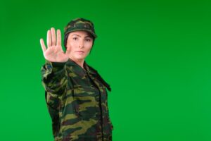 A young female soldier in military attire stands against a green backdrop, signaling a stop to the camera with ample blank space on the side.