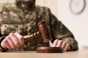 In a law concept image, a close-up shows a man in a military uniform sitting at a table indoors, holding a gavel.